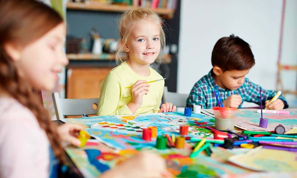Estudiantes de primaria participando en un taller de pintura con materiales artísticos y colores en el aula.